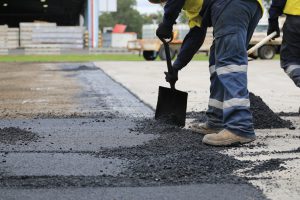 Man moving asphalt with shovel